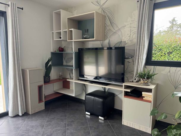 Meuble TV sur mesure avec rangements ouverts et fermés, étagères asymétriques, décorations modernes, et finition en bois clair, intégrant un coin multimédia fonctionnel et esthétique.