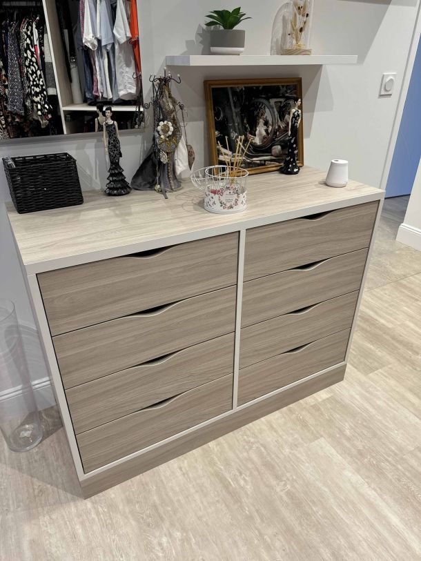 Commode sur mesure avec tiroirs en finition bois clair, décorée avec des objets, un miroir et des accessoires, placée dans un dressing moderne avec un sol en parquet.